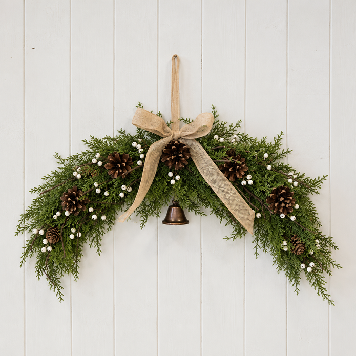 White berry arched Christmas swag with hessian bow and bell against light painted panelling