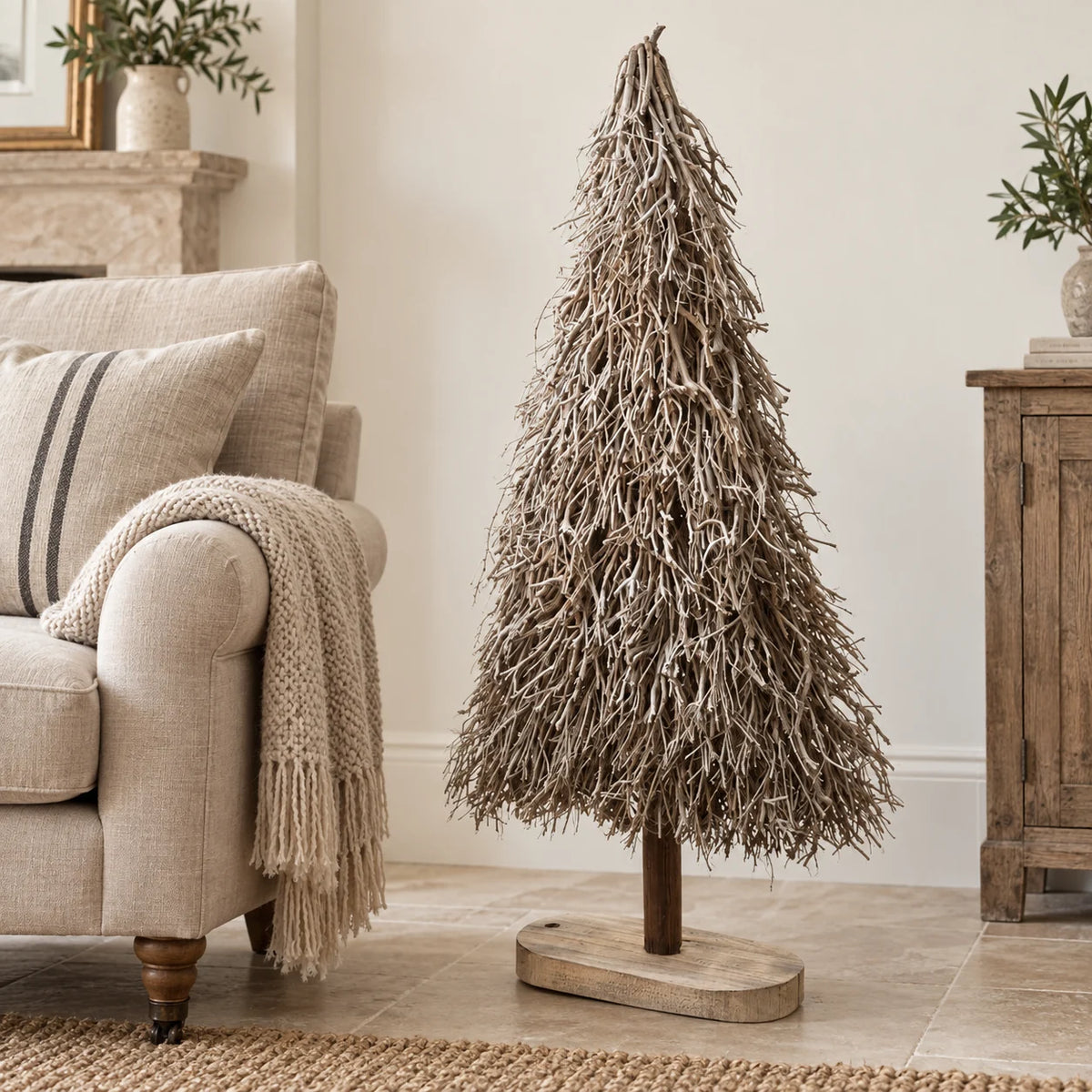 Standing white and natural twig tree beside a linen armchair.