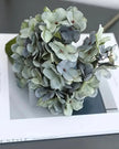 Artificial short dusky blue hydrangea stem from Starlight Express, featuring vibrant blue blooms and realistic foliage.