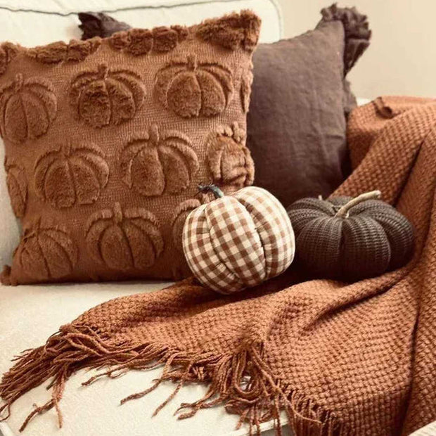 Decorative pillows with pumpkin pattern on a couch with a blanket and pumpkins.
