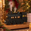 Black steam train oil diffuser with glowing windows and mist beside Christmas decorations