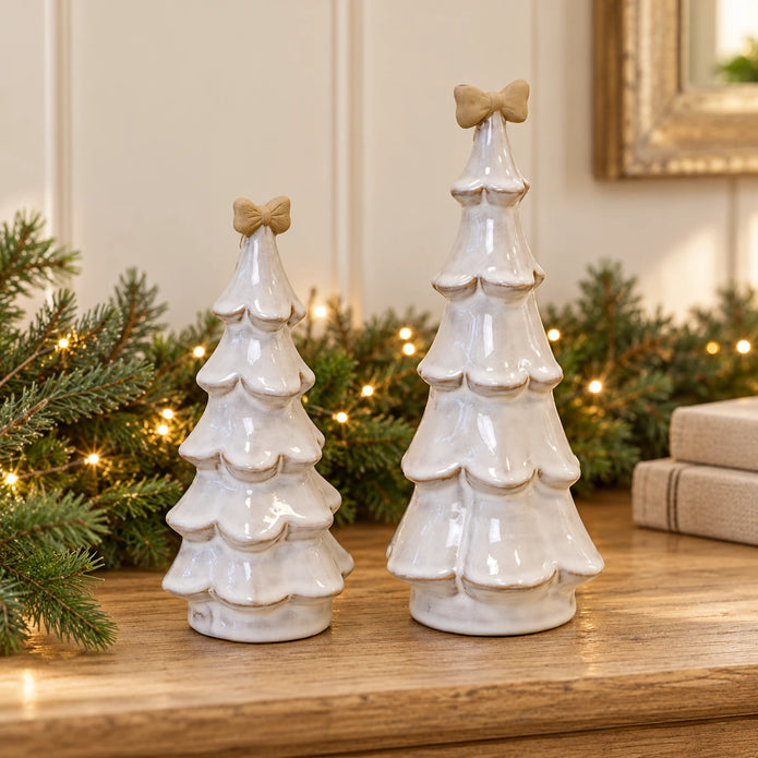 Medium and large stone-glazed ceramic Christmas trees with cream bows, on an oak console with Christmas greenery.
