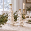 Medium and large stone-glazed ceramic Christmas trees with cream bows, on a Christmas dining table.
