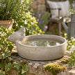 Stoneware bird bath bowl with sculpted bird filled with water in a cottage garden