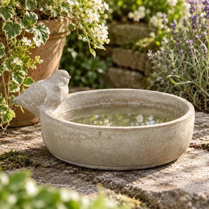 Stoneware bird bath with decorative bird on rim among garden flowers and lavender
