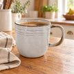 Pale stoneware coffee mug with brown rim on an oak counter in a light country kitchen