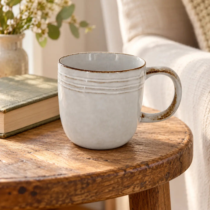 Pale glazed stoneware mug beside a book in a neutral reading corner