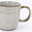 Close-up of the stoneware coffee mug's raised bands, brown rim and glazed handle