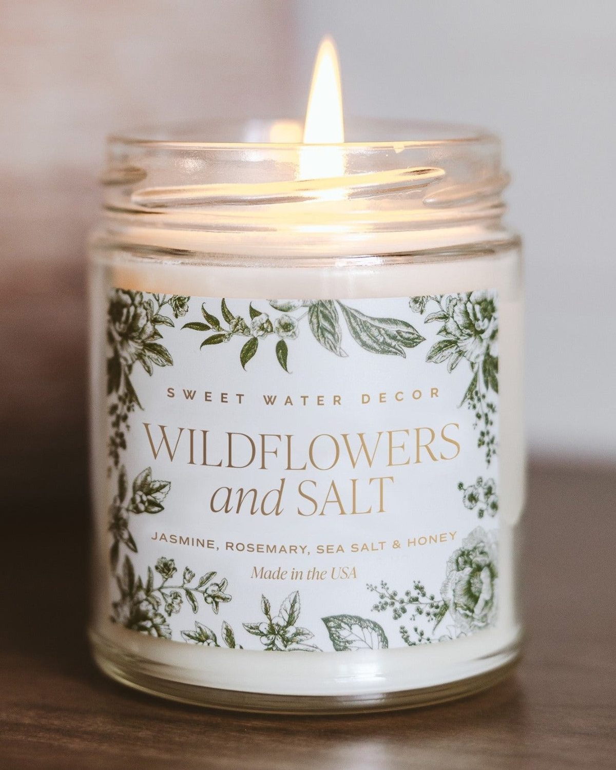 Clear glass candle jar by Sweet Water Decor with wildflowers and salt inside, showcasing a decorative and rustic aesthetic.