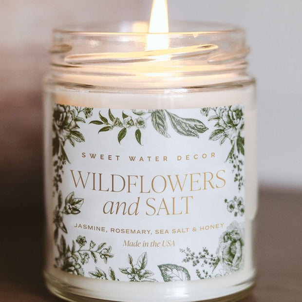 Clear glass candle jar by Sweet Water Decor with wildflowers and salt inside, showcasing a decorative and rustic aesthetic.