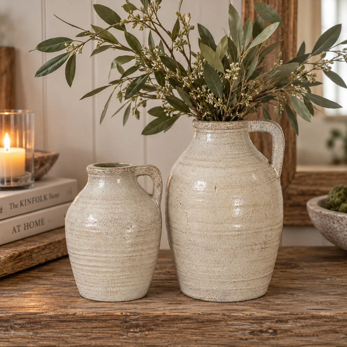 Tarn neutral stone glazed jugs in two sizes with large jug holding leafy olive branches on wooden sideboard