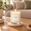 Heaven Scent Tea Tree And Geranium Medium Candle, lit in clear glass on a stone coaster in a living room