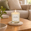 Heaven Scent Tea Tree And Geranium Small Candle, lit in clear glass on a stone coaster in a living room