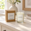Heaven Scent Tea Tree And Geranium Small Candle, unlit with its brown kraft box on a cream console