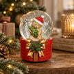 Teddy bear Christmas snow globe with Santa hat and red gift box base styled beside festive greenery and candlelight