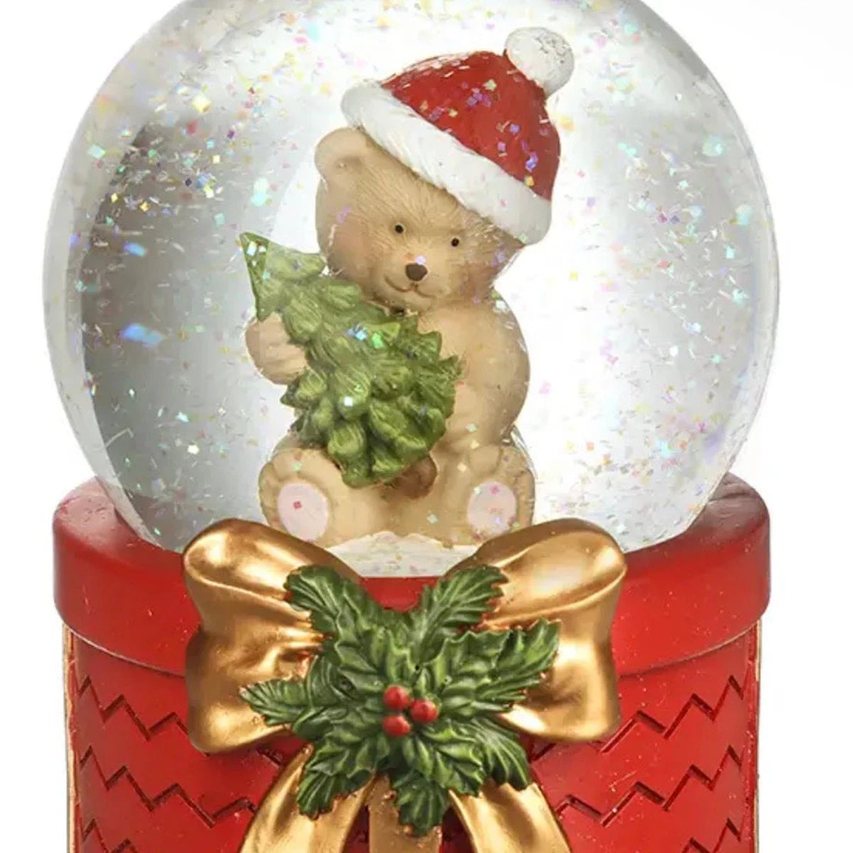 Close-up of teddy bear inside glitter snow globe with red base, gold bow and holly