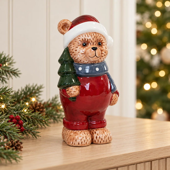 Teddy bear in traditional red holding a green tree, styled on a Christmas console
