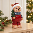 Teddy bear in traditional red holding a green tree, styled on a Christmas console