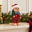 Red Christmas teddy bear ornament on a mantel with evergreen garland