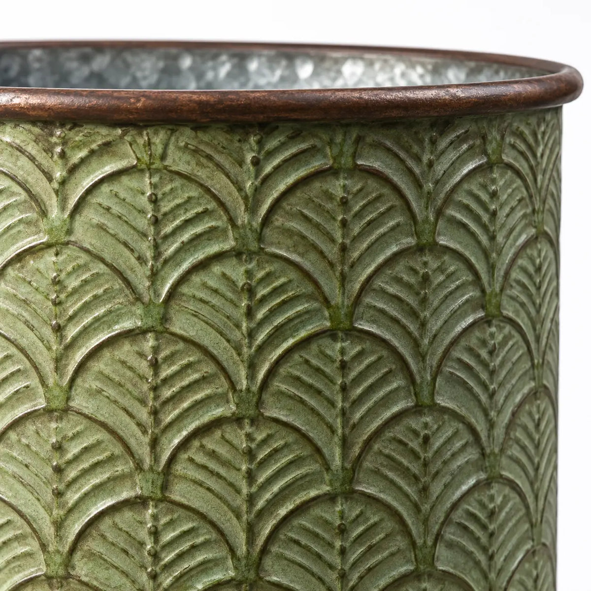 Close-up of the brown rolled rim and embossed leaf pattern on a vintage green metal planter