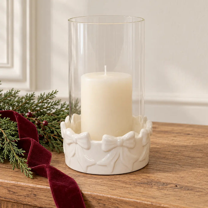 White bow hurricane candle holder with unlit ivory candle on an oak Christmas console