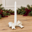 White ceramic bow candle holder with an unlit white taper and Christmas greenery in the background