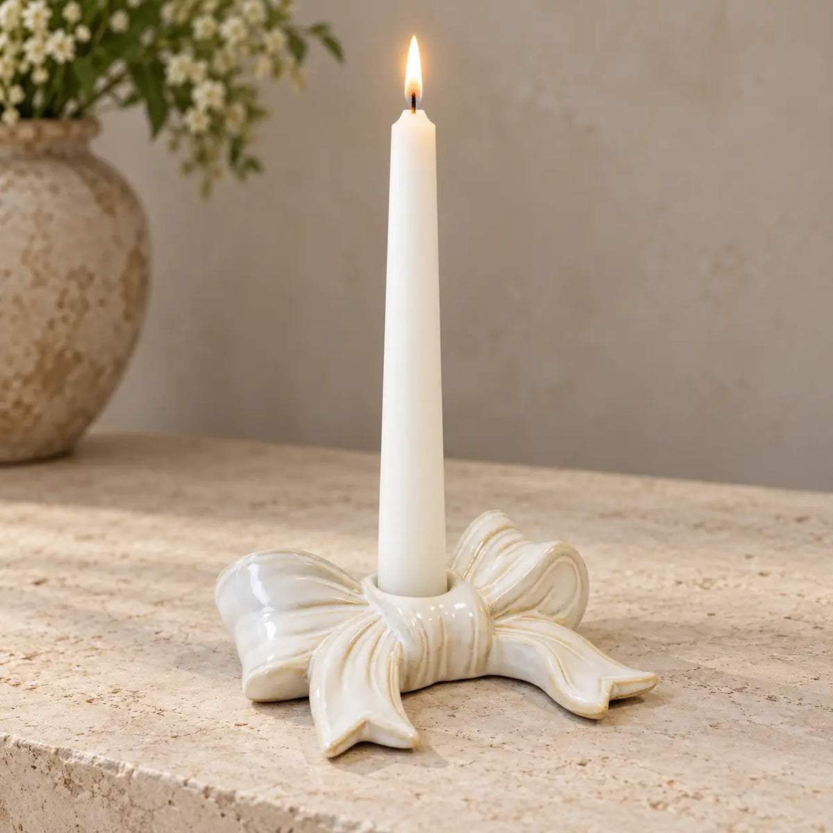 White ceramic bow candlestick with a lit white dinner candle on a pale stone console