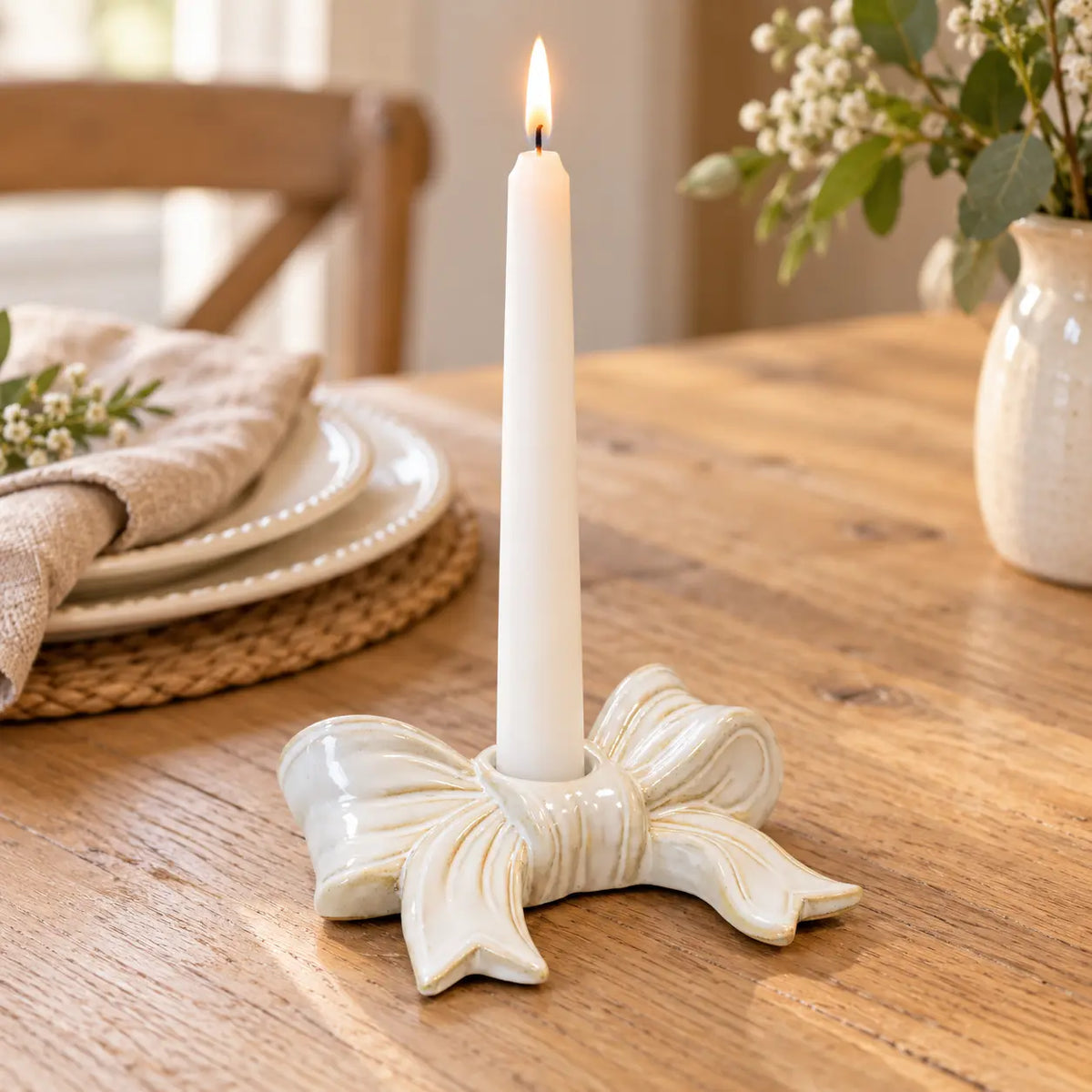 White ceramic bow dinner candle holder with a lit white taper on an oak dining table