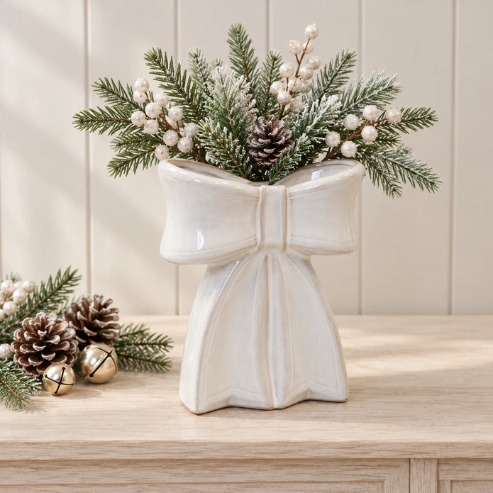 Large white ceramic bow vase with fir and white berries on a pale wood console