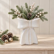 Large white ceramic bow vase with fir and white berries on a pale wood console