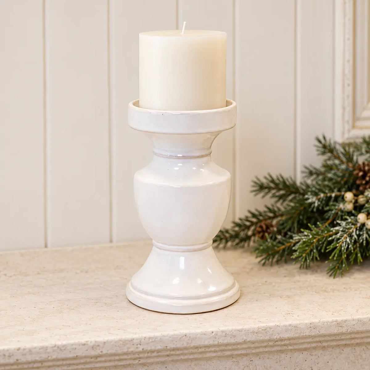 White ceramic pedestal candle holder with unlit candle on a pale stone mantel