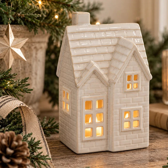 White glazed ceramic tiled light-up house surrounded by natural greenery and warm Christmas lights