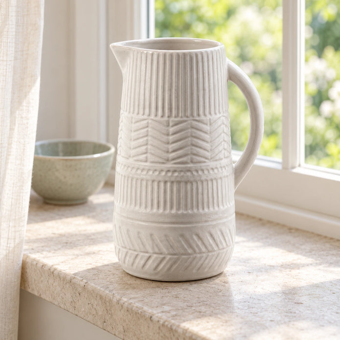 Large white ceramic jug on a sunlit kitchen windowsill showing its textured bands and curved handle.