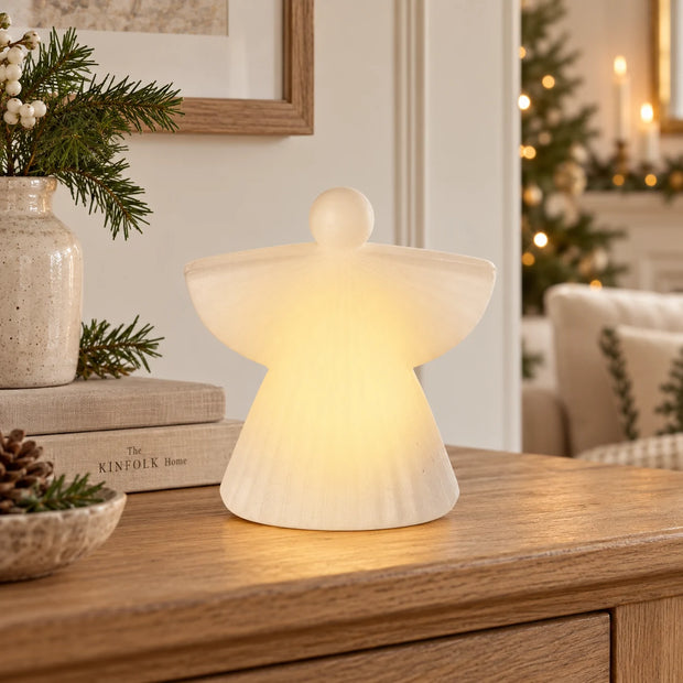 White ceramic LED angel glowing on an oak console.