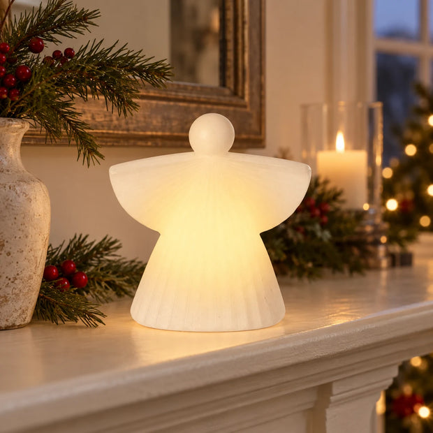 White ceramic LED angel on a cream mantel at dusk.