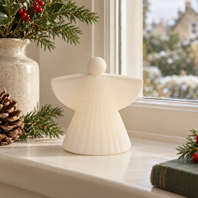 White ceramic angel on a cream windowsill in daylight.