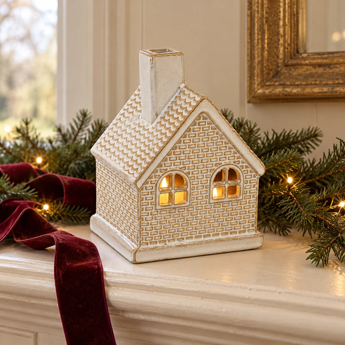 White ceramic LED Christmas cottage by Satchville, lit up for festive holiday decor on a mantel.