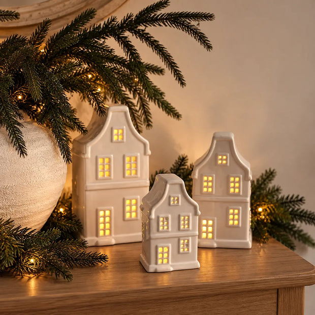 Three sizes of glowing white ceramic Dutch house ornaments with evergreen styling