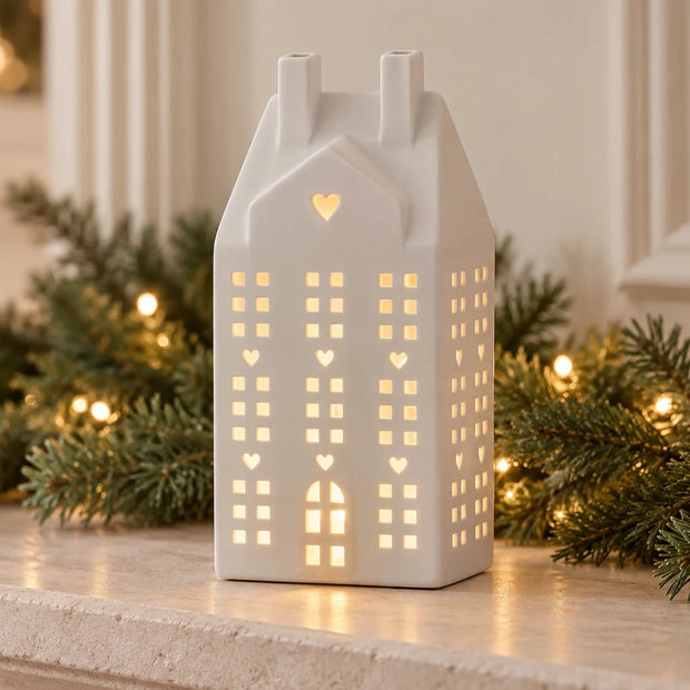 White ceramic LED house with heart windows glowing on a Christmas mantel