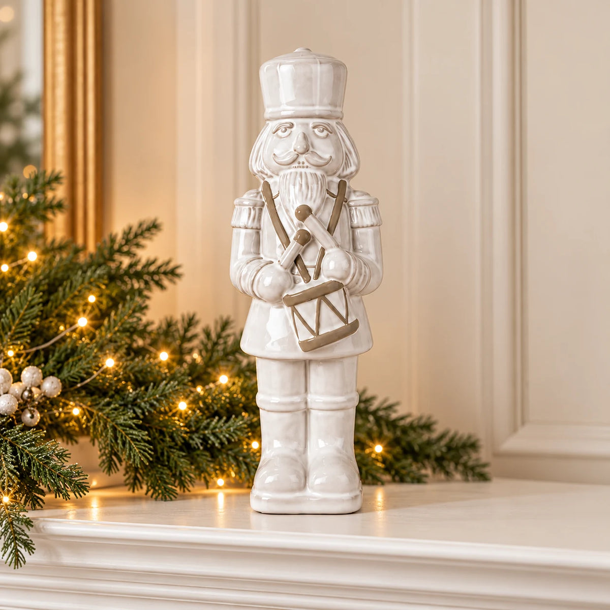 33cm large white glazed ceramic nutcracker drummer on a Christmas mantel with green foliage