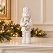 26cm medium white glazed ceramic nutcracker drummer on a Christmas mantel with green foliage