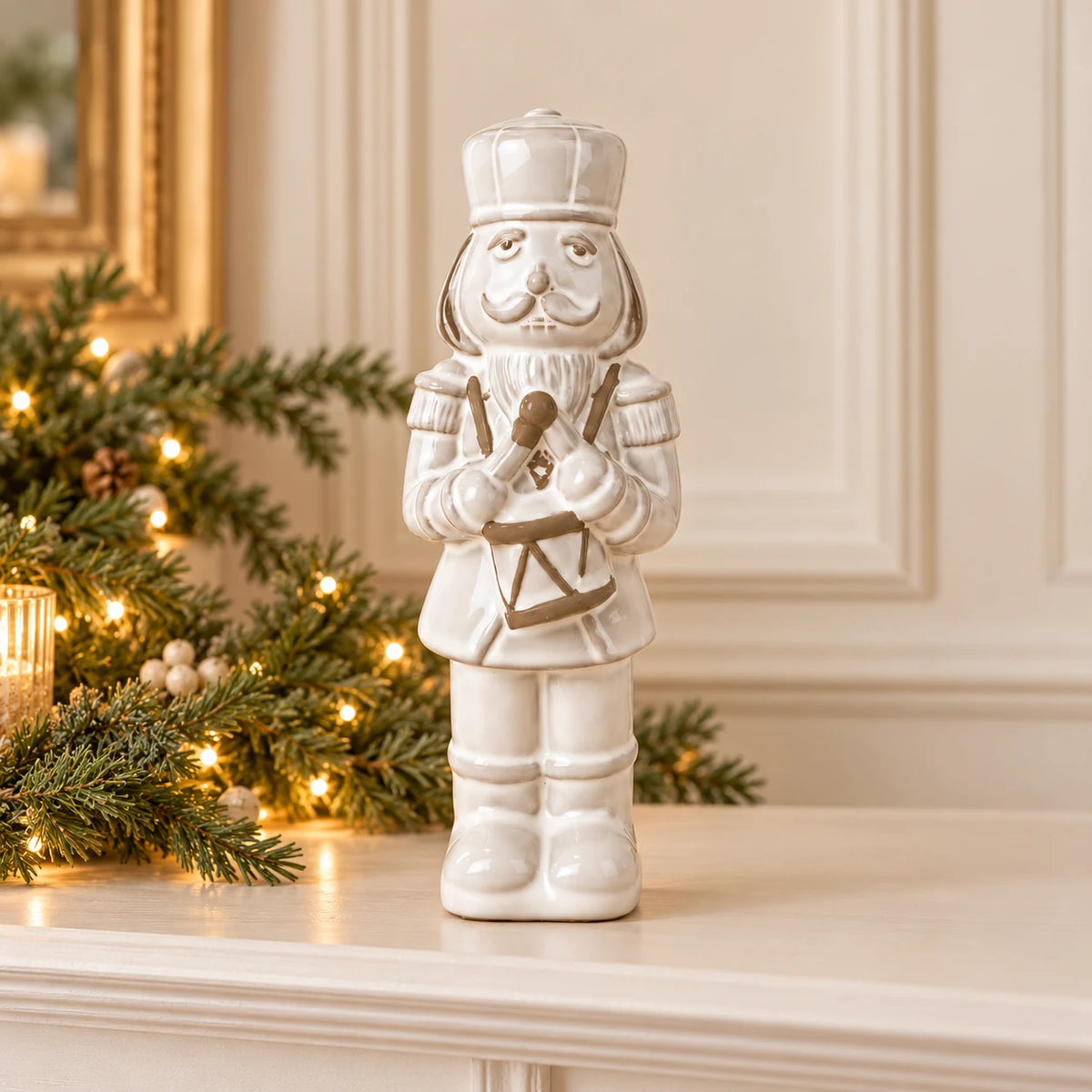 21cm small white glazed ceramic nutcracker drummer on a Christmas mantel with green foliage