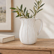Large white ceramic petal jug with olive stems on a wooden dresser
