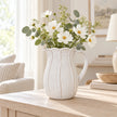 Large white ceramic petal jug with white flowers on a pale oak console