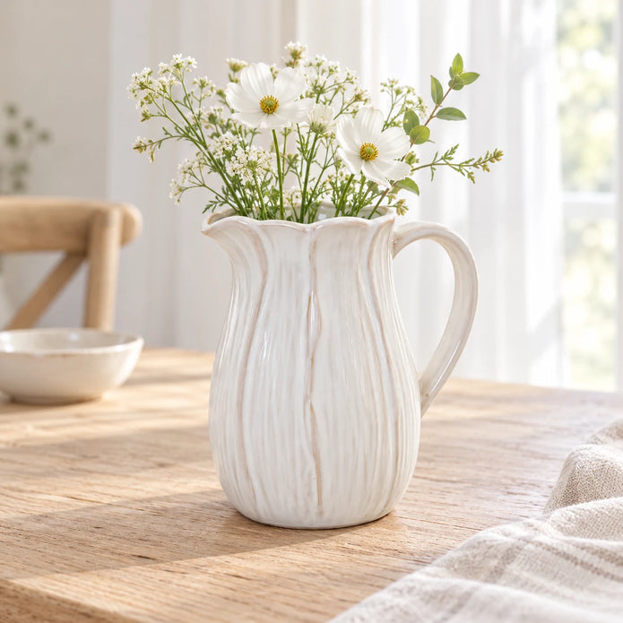 Large white ceramic petal jug with white meadow flowers on a pale oak breakfast table