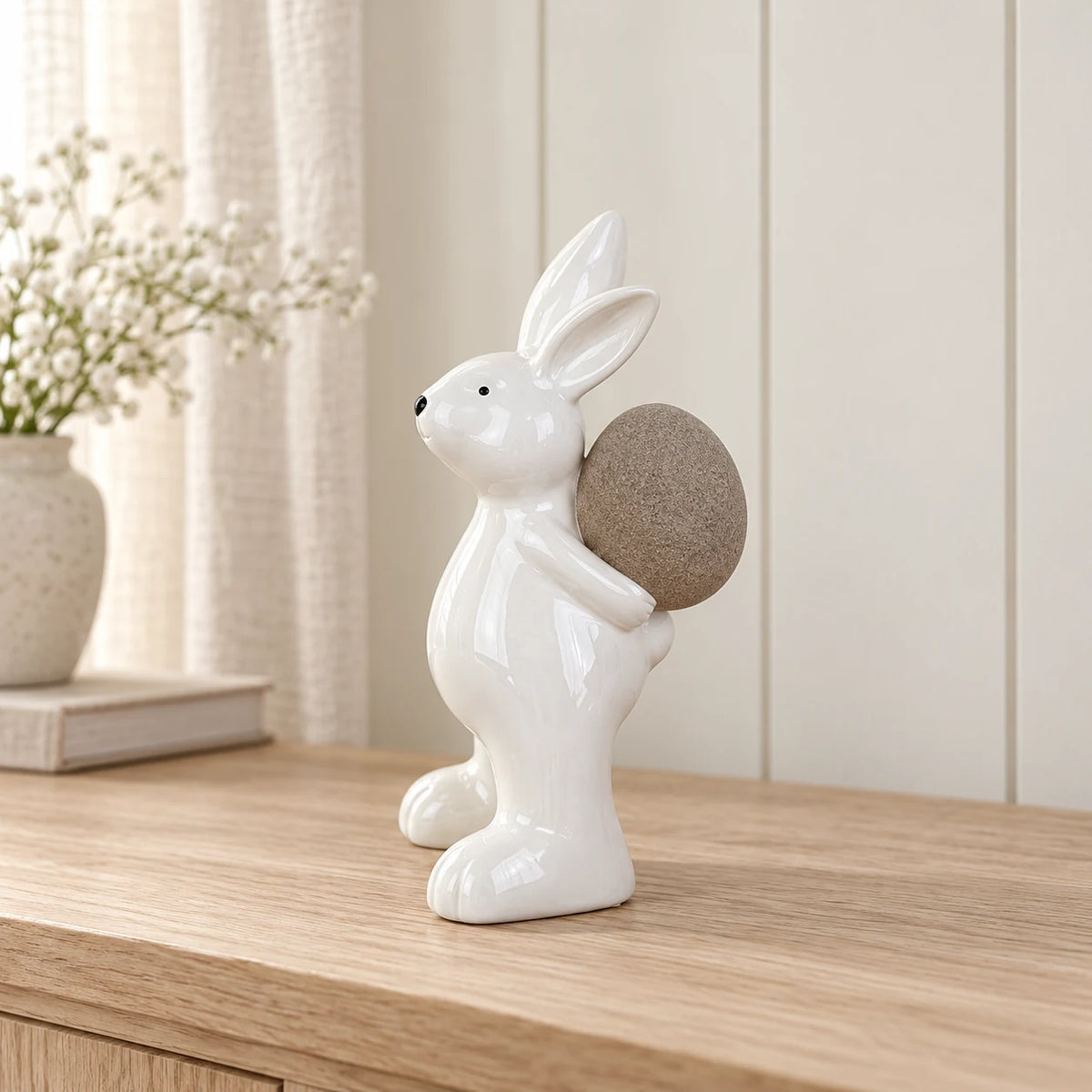 Large white ceramic rabbit holding a taupe egg, 21cm tall, on a pale oak console in a neutral interior.