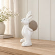 Large white ceramic rabbit holding a taupe egg, 21cm tall, on a pale oak console in a neutral interior.