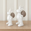 White ceramic rabbits carrying textured taupe eggs, small 18cm and large 21cm shown side by side for size comparison; sold separately.