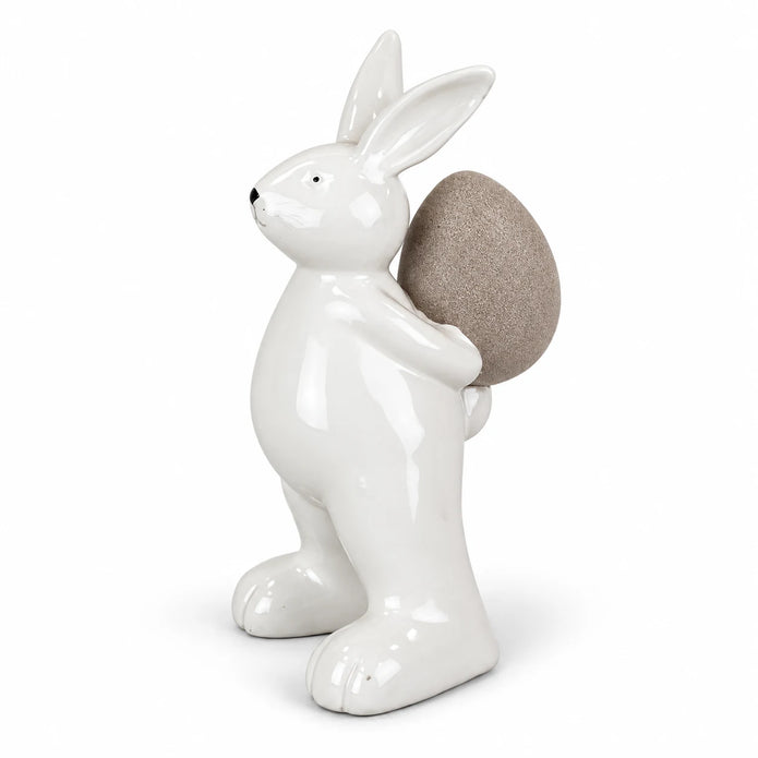 Small white ceramic rabbit holding a taupe egg, 18cm tall, complete ornament on a white studio background.