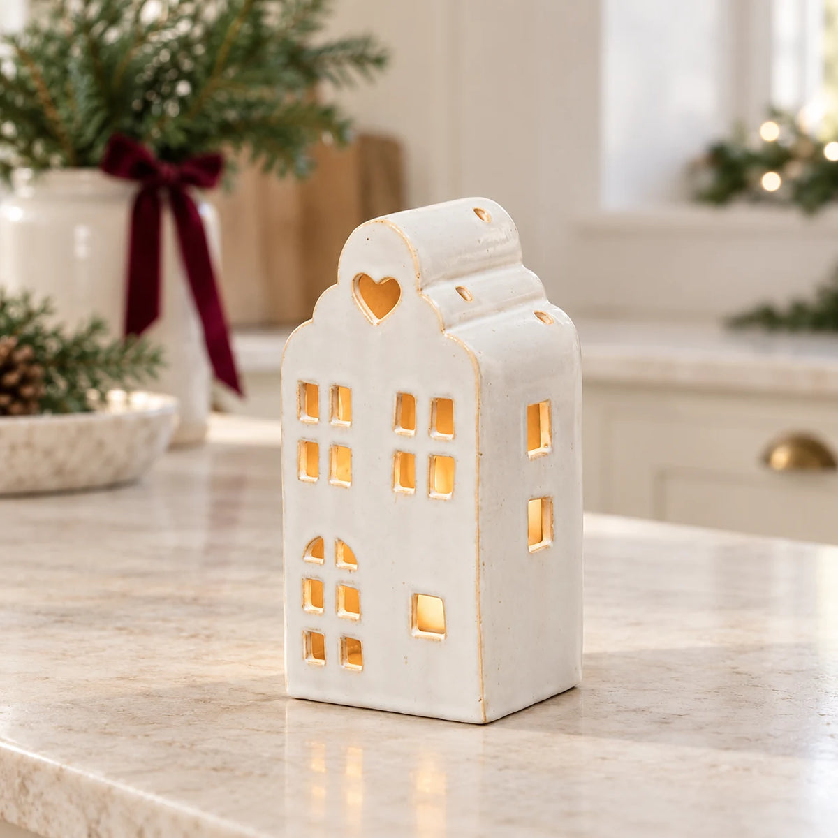 White ceramic townhouse tealight holder with heart opening styled on a light Christmas kitchen worktop